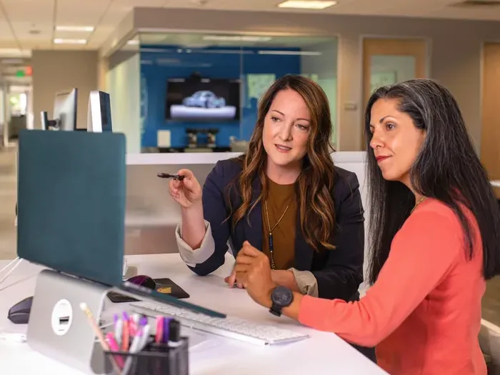 Two women in a modern office talking and pointing at a computer screen during a planning session, featured on Urban Biz Directory